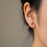 Close-up of an ear wearing a small green earring against a neutral background