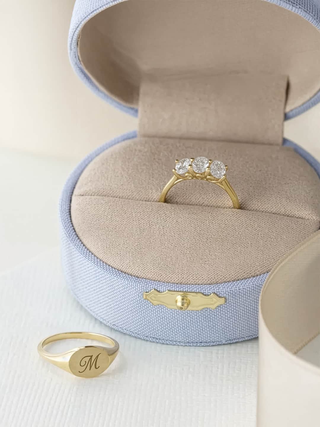 Gold diamond three stone ring displayed in open linen jewelry box on white background