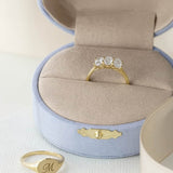 Gold diamond three stone ring displayed in open linen jewelry box on white background
