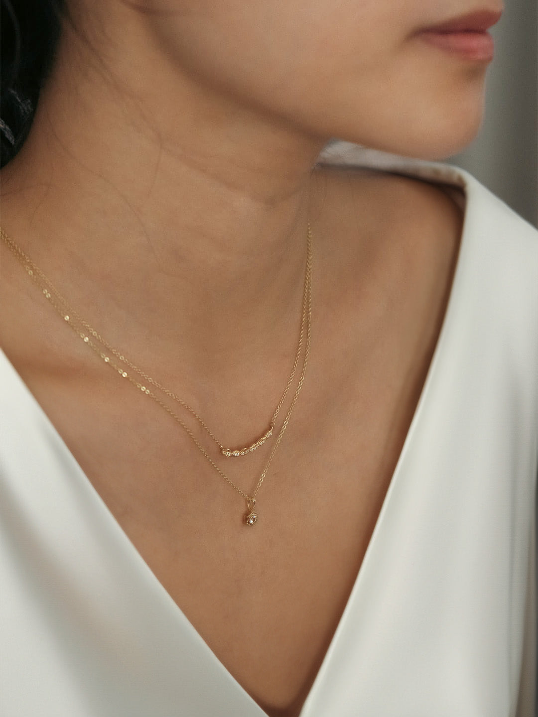 A close-up image of a woman wearing a white sapphire necklace with a gold finish and hexagon shape.