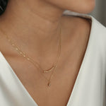 A close-up image of a woman wearing a white sapphire necklace with a gold finish and hexagon shape.