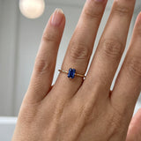 Hand wearing a gold ring with a blue gemstone against a neutral background