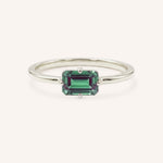 White gold solitaire ring with emerald-cut alexandrite gemstone on white background