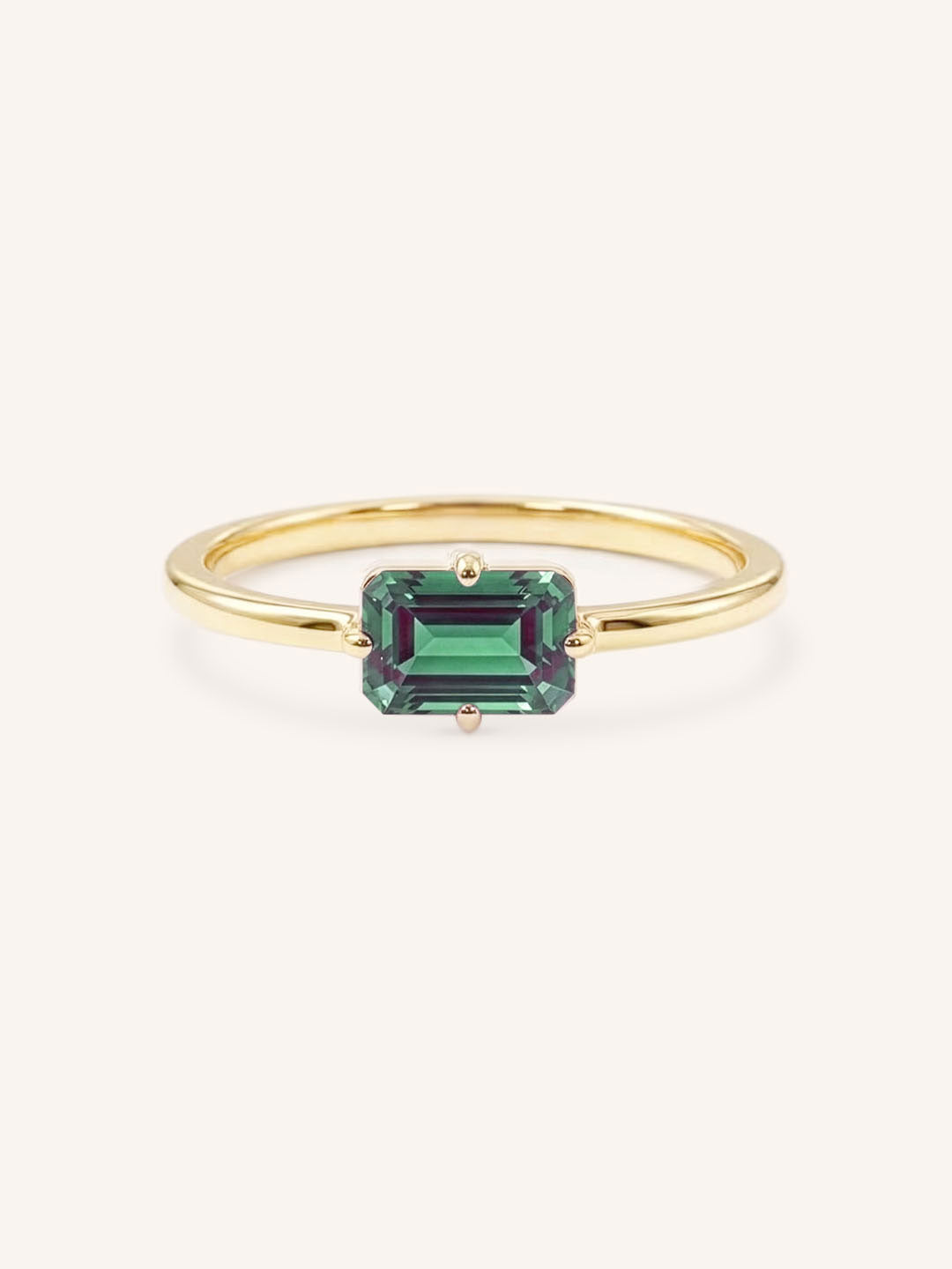 Yellow gold solitaire ring with emerald-cut alexandrite gemstone on white background
