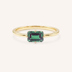 Yellow gold solitaire ring with emerald-cut alexandrite gemstone on white background