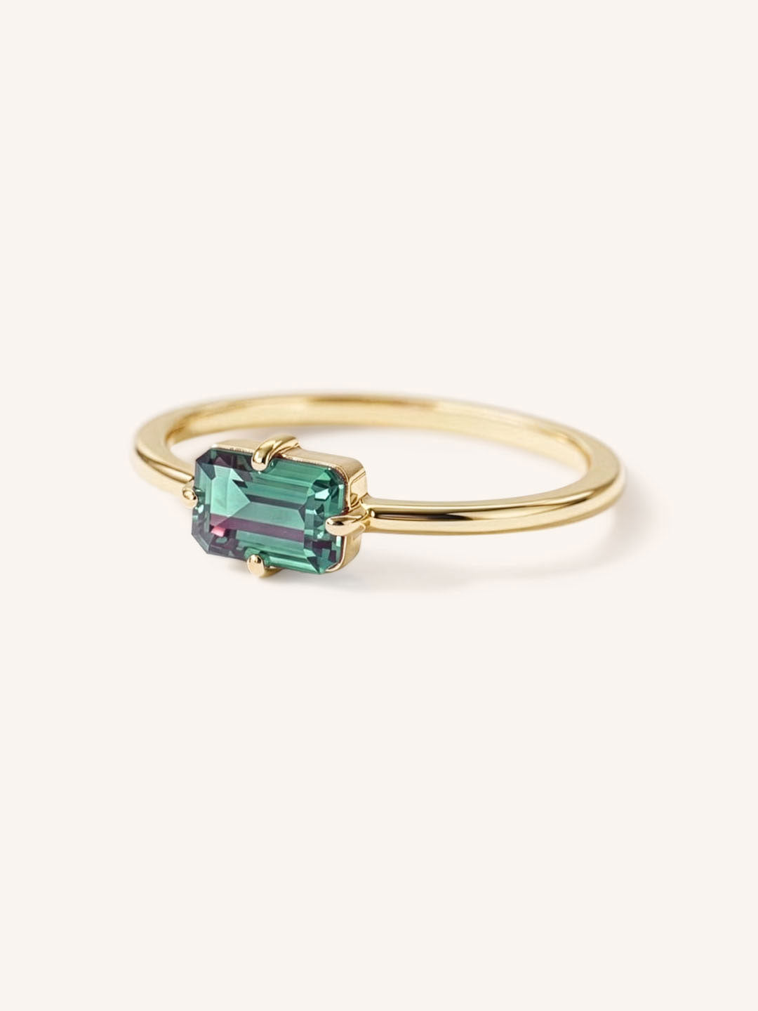 Yellow gold solitaire ring with emerald-cut alexandrite gemstone, side view on white background