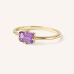 Yellow gold solitaire ring with emerald-cut amethyst gemstone, side view on white background