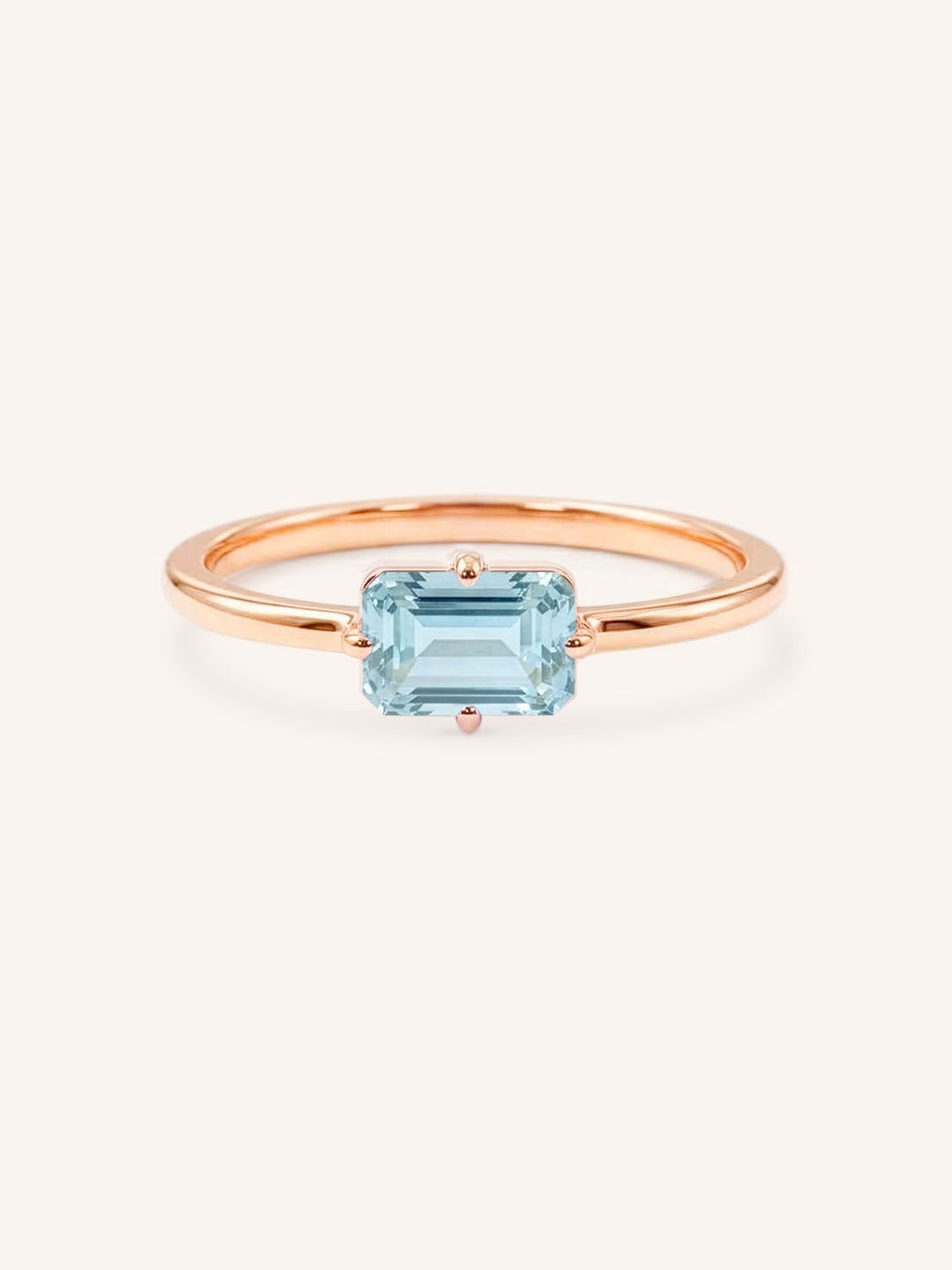 Rose gold solitaire ring with emerald-cut aquamarine gemstone on white background