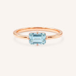 Rose gold solitaire ring with emerald-cut aquamarine gemstone on white background
