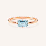 Rose gold solitaire ring with emerald-cut aquamarine gemstone on white background