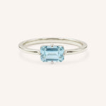 White gold solitaire ring with emerald-cut aquamarine gemstone on white background