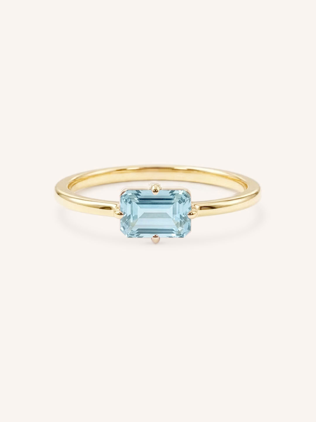 Yellow gold solitaire ring with emerald-cut aquamarine gemstone on white background