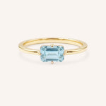 Yellow gold solitaire ring with emerald-cut aquamarine gemstone on white background