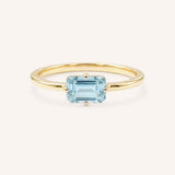 Yellow gold solitaire ring with emerald-cut aquamarine gemstone on white background