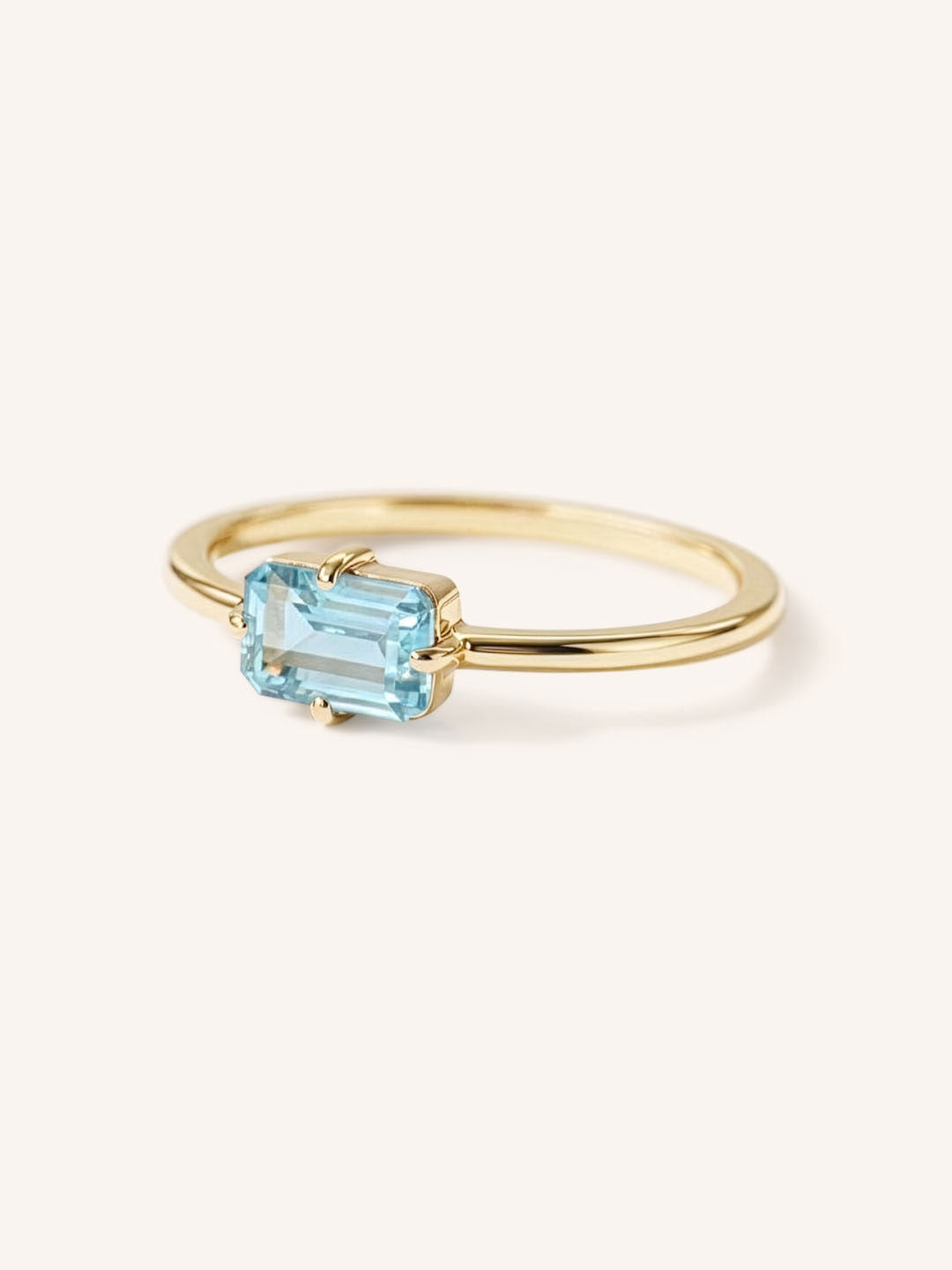 Yellow gold solitaire ring with emerald-cut aquamarine gemstone, side view on white background