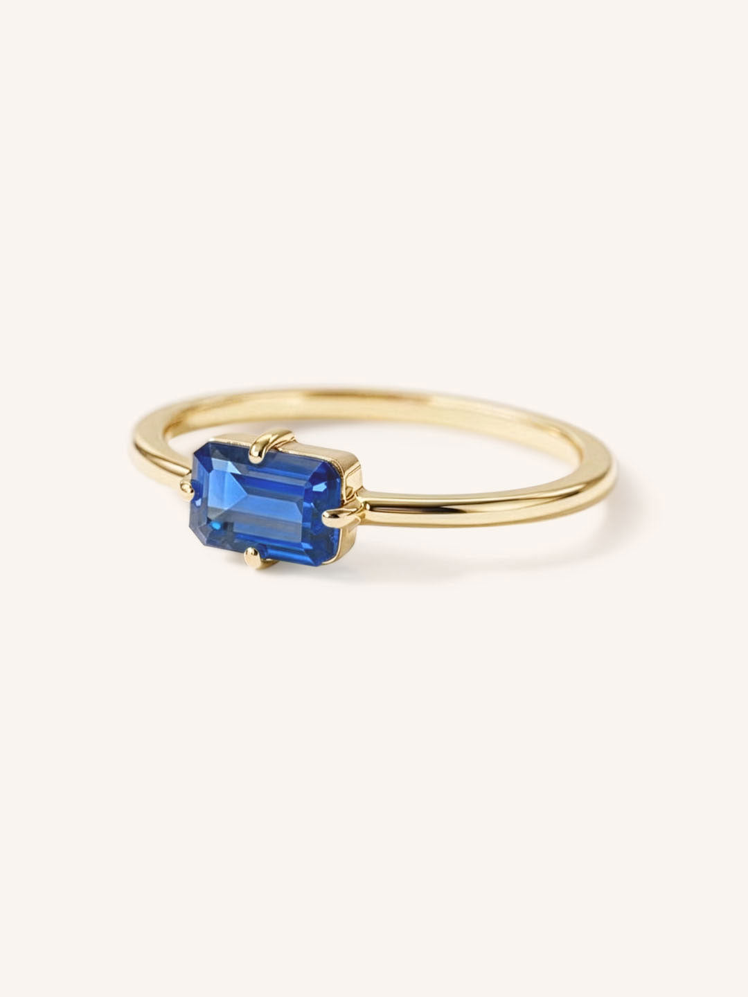 Yellow gold solitaire ring with emerald-cut blue sapphire gemstone, side view on white background