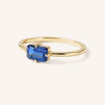 Yellow gold solitaire ring with emerald-cut blue sapphire gemstone, side view on white background