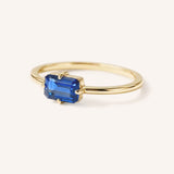 Yellow gold solitaire ring with emerald-cut blue sapphire gemstone, side view on white background