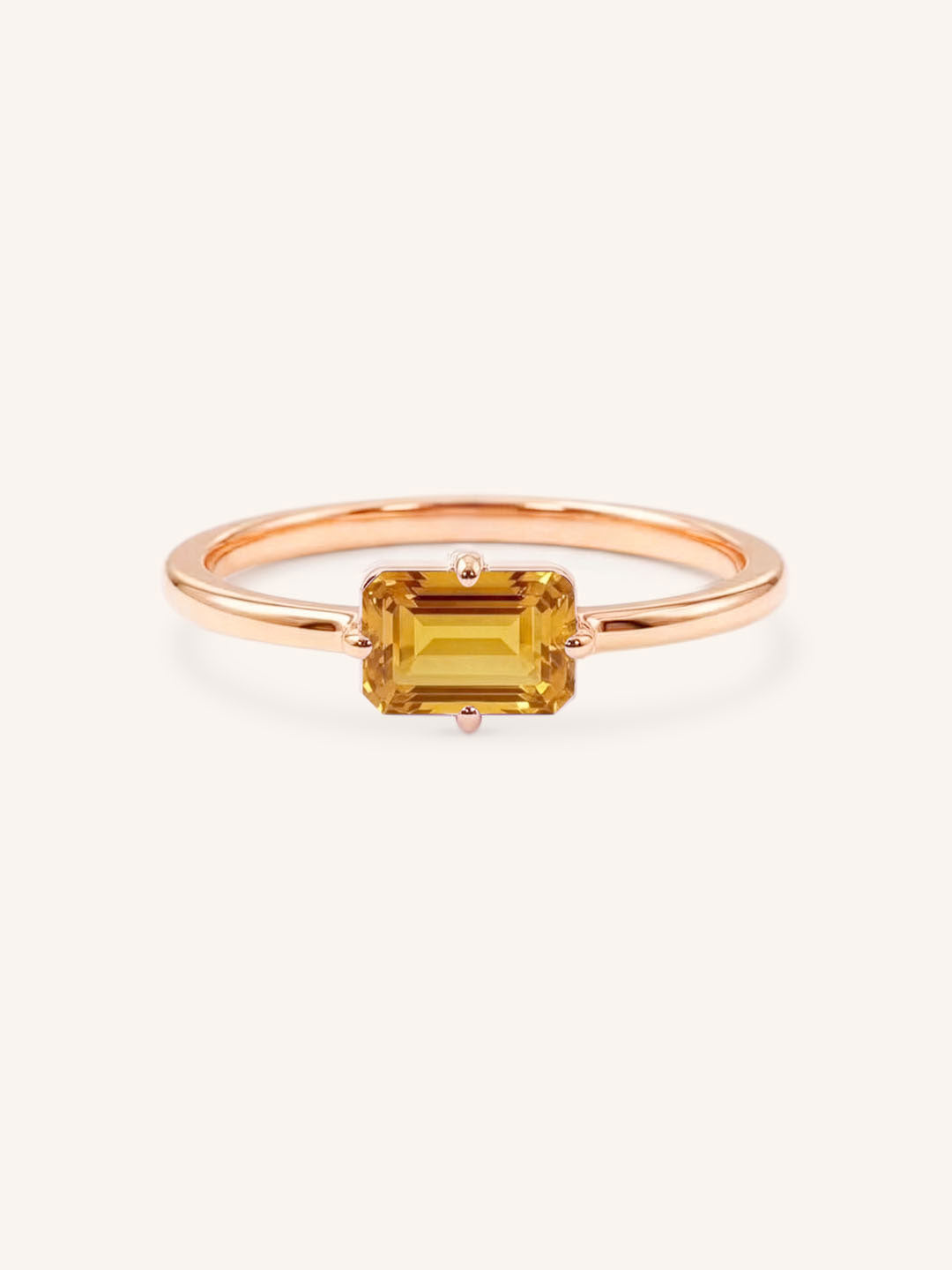 Rose gold solitaire ring with emerald-cut citrine gemstone on white background
