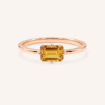 Rose gold solitaire ring with emerald-cut citrine gemstone on white background