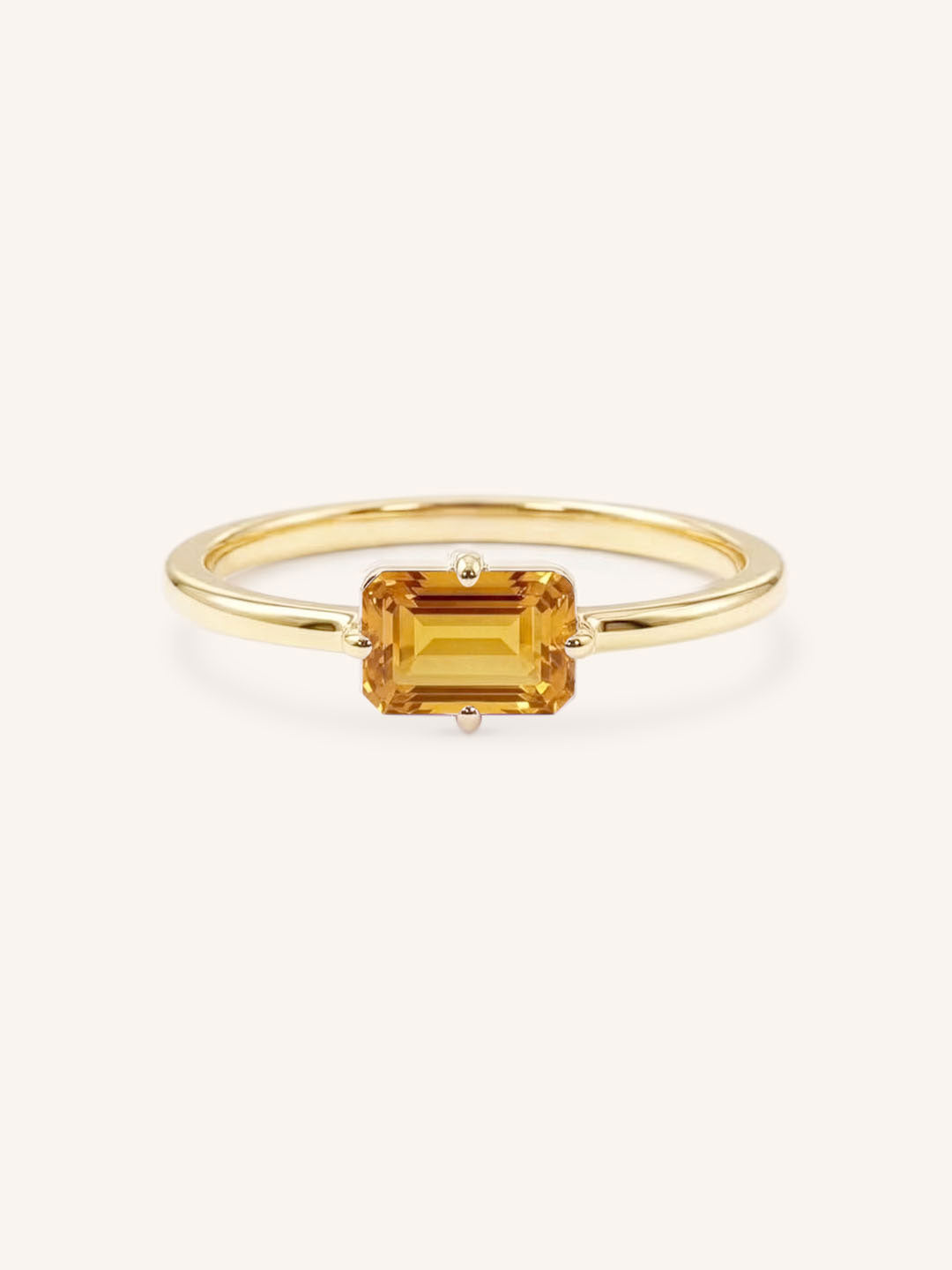 Yellow gold solitaire ring with emerald-cut citrine gemstone on white background