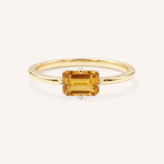 Yellow gold solitaire ring with emerald-cut citrine gemstone on white background