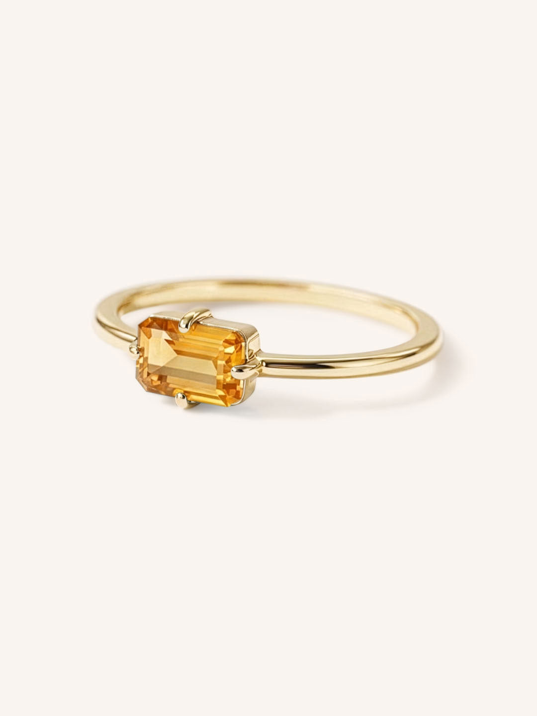 Yellow gold solitaire ring with emerald-cut citrine gemstone, side view on white background