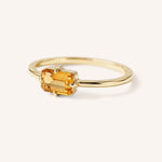 Yellow gold solitaire ring with emerald-cut citrine gemstone, side view on white background