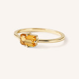 Yellow gold solitaire ring with emerald-cut citrine gemstone, side view on white background