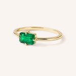 Yellow gold solitaire ring with emerald-cut emerald gemstone, side view on white background