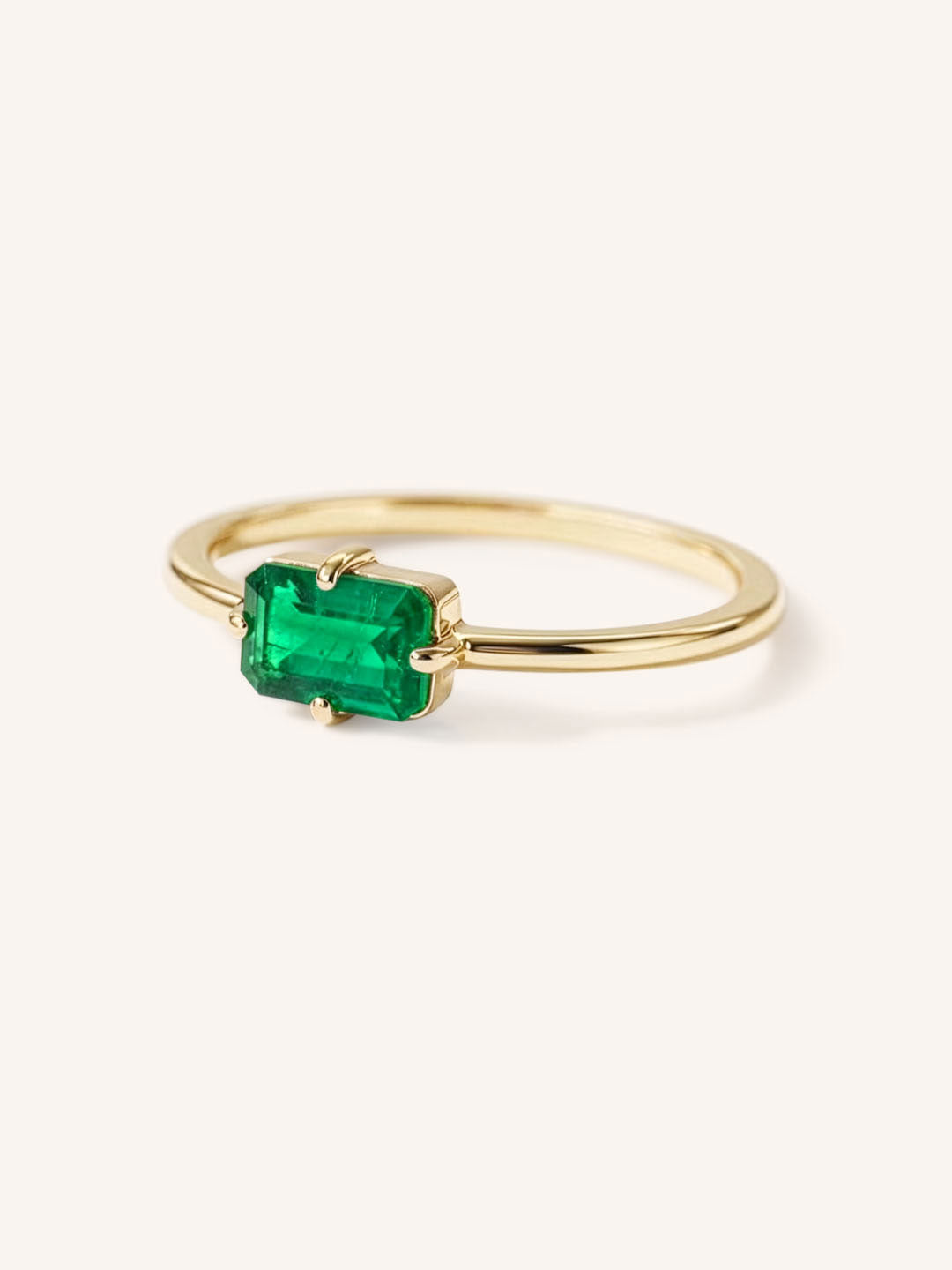 Yellow gold solitaire ring with emerald-cut emerald gemstone, side view on white background