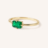 Yellow gold solitaire ring with emerald-cut emerald gemstone, side view on white background