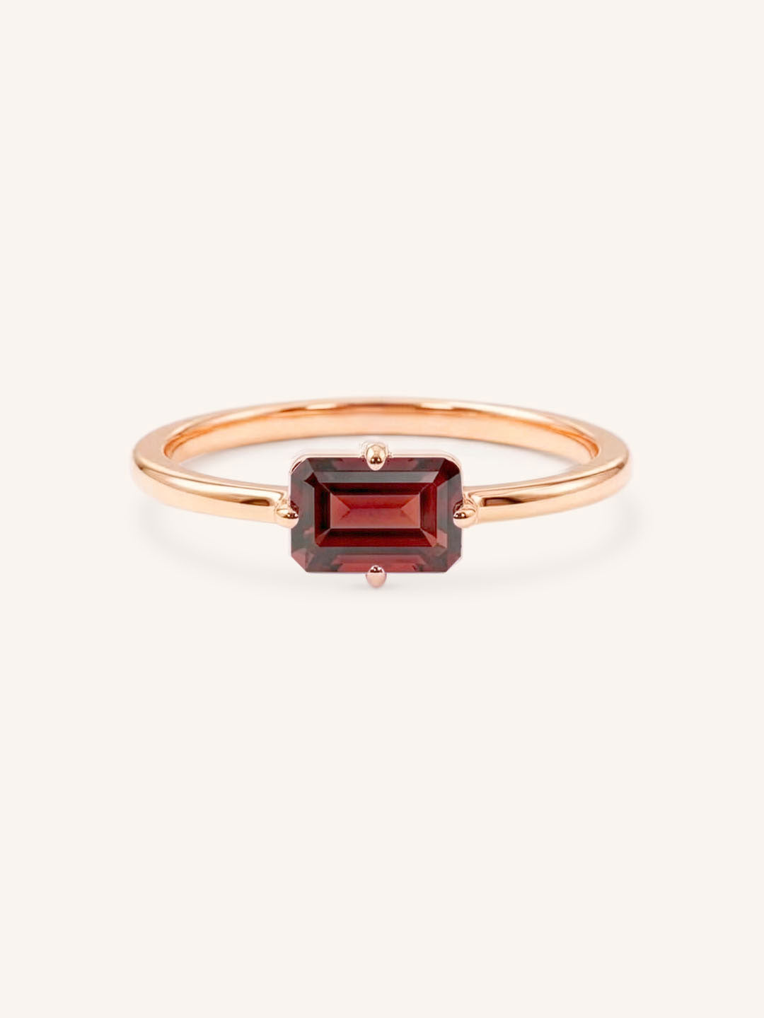Rose gold solitaire ring with emerald-cut garnet gemstone on white background