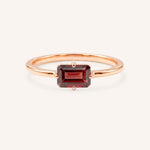 Rose gold solitaire ring with emerald-cut garnet gemstone on white background