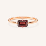 Rose gold solitaire ring with emerald-cut garnet gemstone on white background