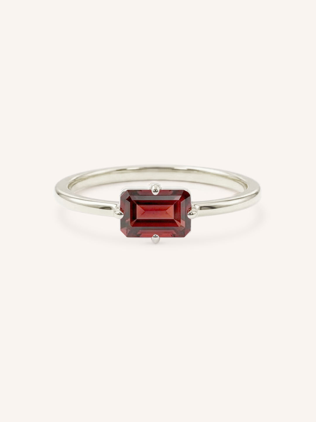 White gold solitaire ring with emerald-cut garnet gemstone on white background