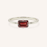 White gold solitaire ring with emerald-cut garnet gemstone on white background