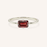 White gold solitaire ring with emerald-cut garnet gemstone on white background