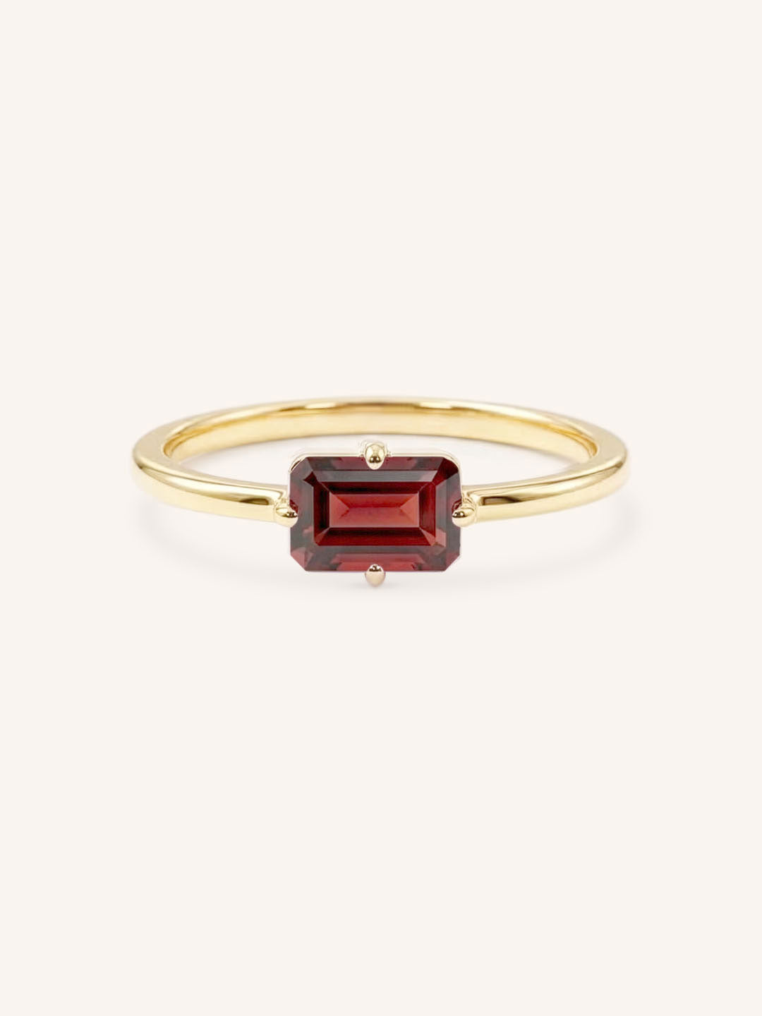Yellow gold solitaire ring with emerald-cut garnet gemstone on white background