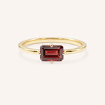 Yellow gold solitaire ring with emerald-cut garnet gemstone on white background