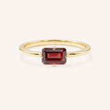 Yellow gold solitaire ring with emerald-cut garnet gemstone on white background