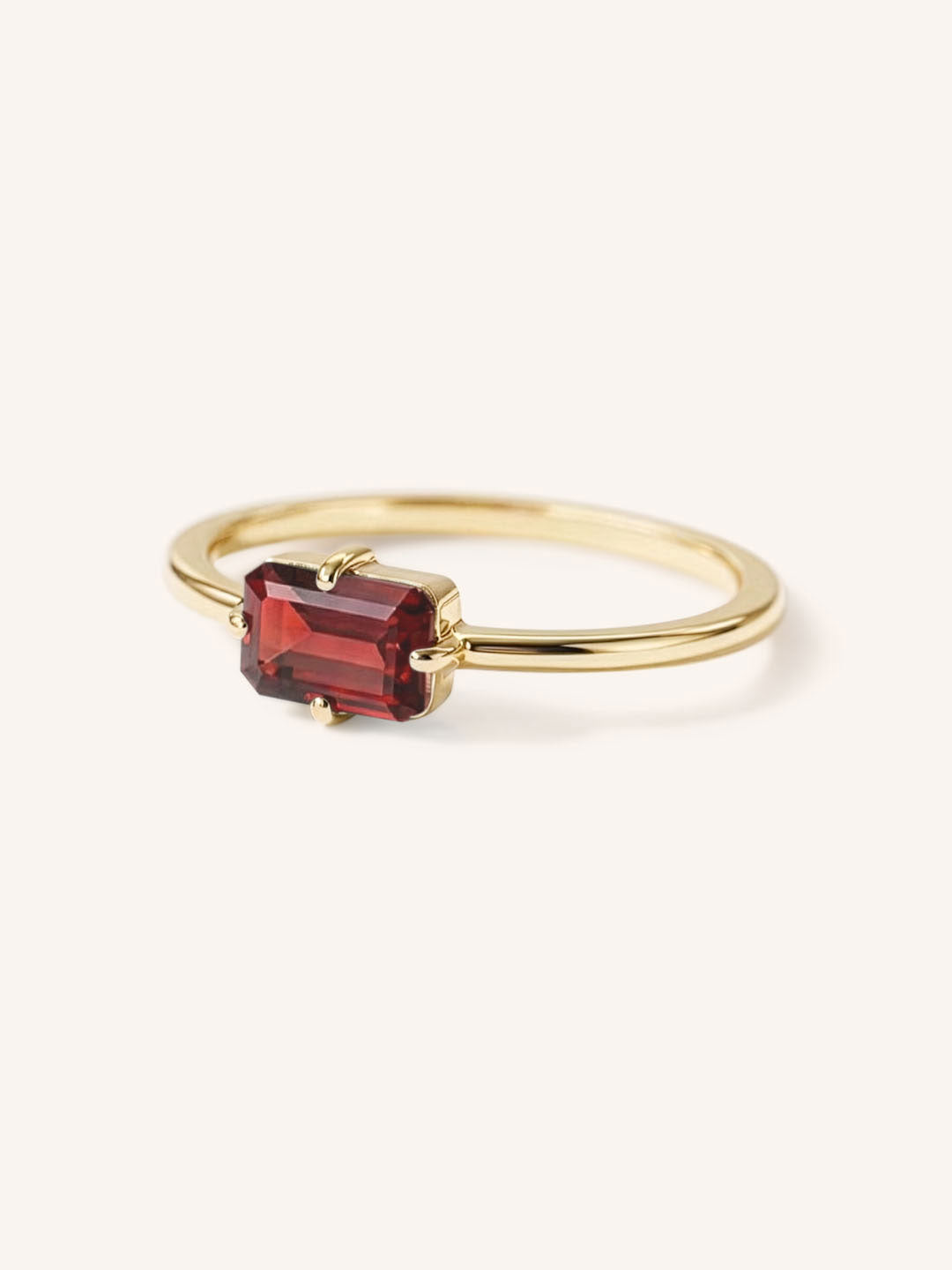 Yellow gold solitaire ring with emerald-cut garnet gemstone, side view on white background