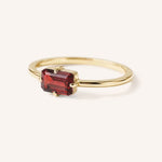 Yellow gold solitaire ring with emerald-cut garnet gemstone, side view on white background