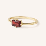 Yellow gold solitaire ring with emerald-cut garnet gemstone, side view on white background