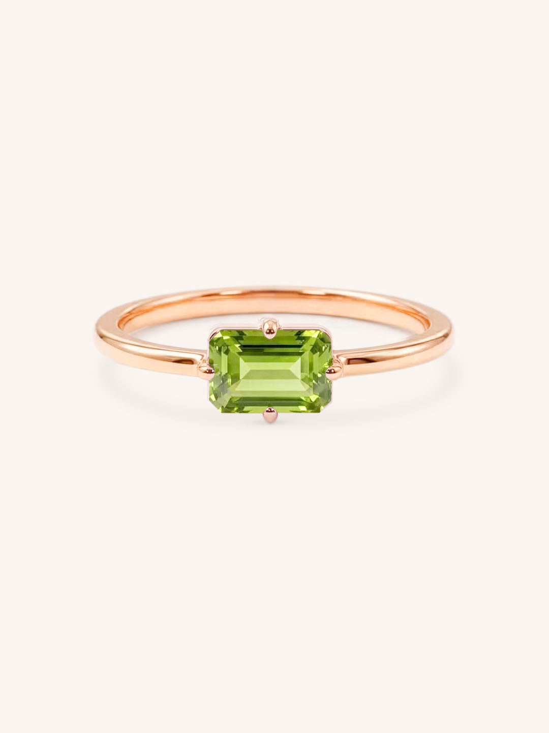 Rose gold solitaire ring with emerald-cut peridot gemstone on white background