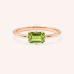 Rose gold solitaire ring with emerald-cut peridot gemstone on white background