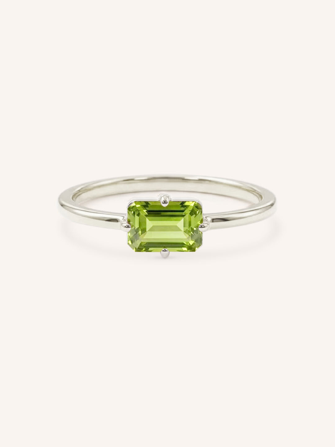 White gold solitaire ring with emerald-cut peridot gemstone on white background