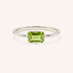 White gold solitaire ring with emerald-cut peridot gemstone on white background