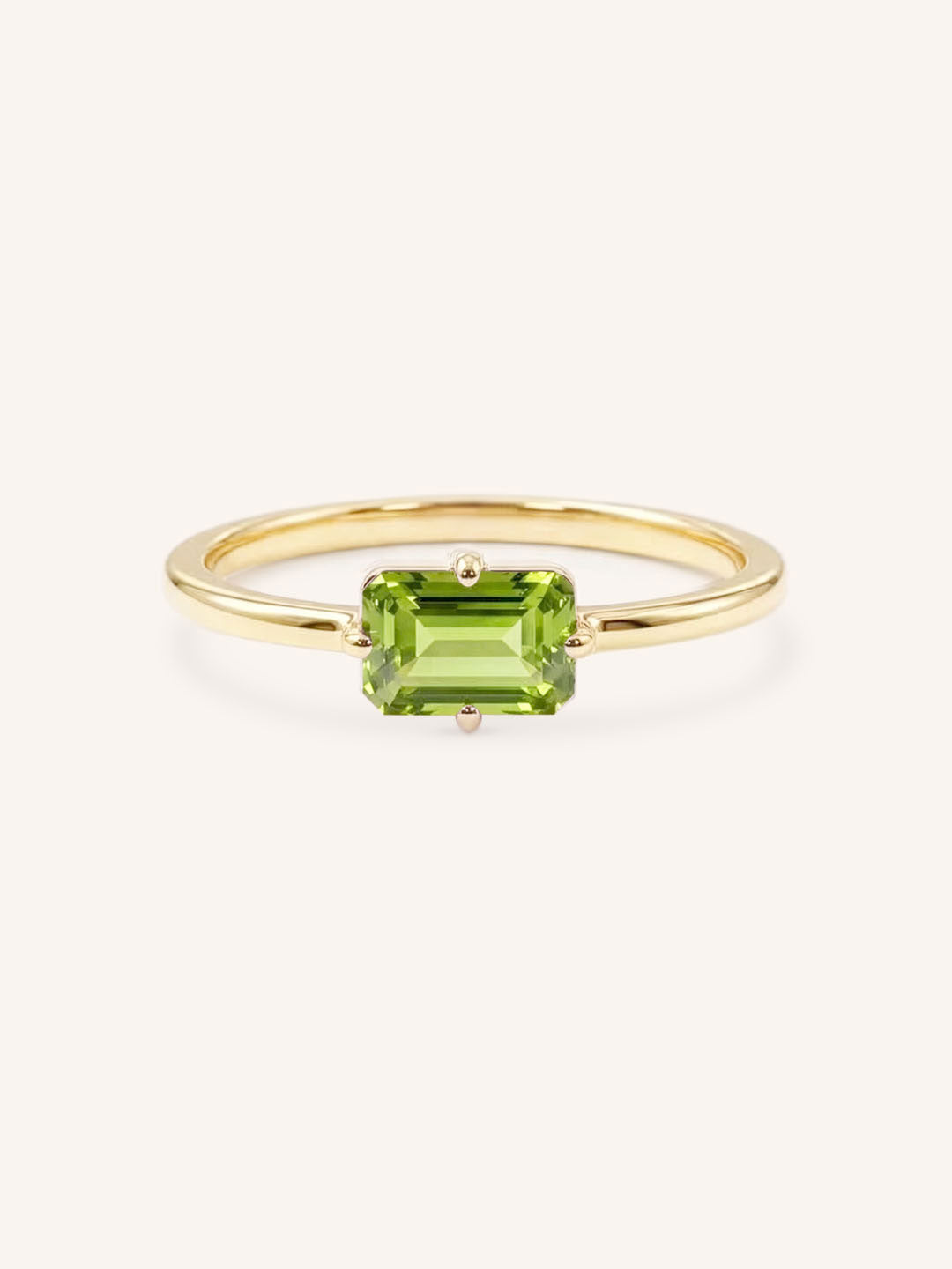 Yellow gold solitaire ring with emerald-cut peridot gemstone on white background