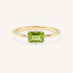 Yellow gold solitaire ring with emerald-cut peridot gemstone on white background